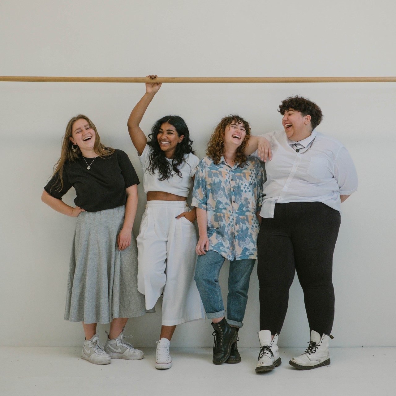 Four people standing in front of white wall laughing