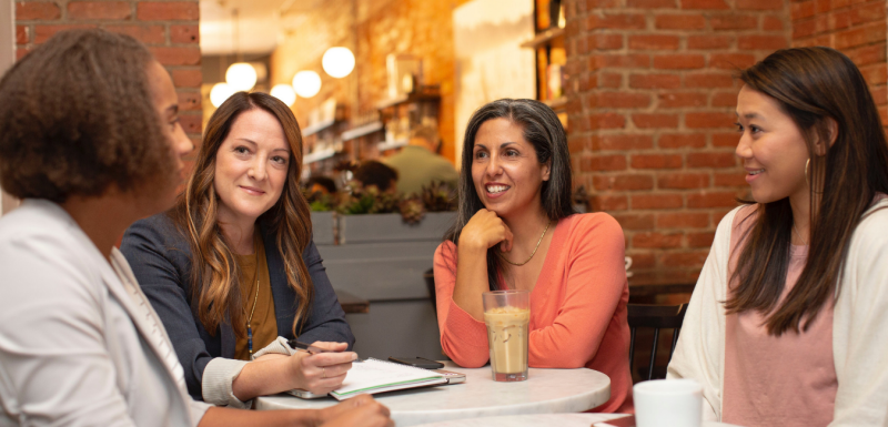 four women sitting around a table talking and smiling